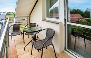 Un balcon doté d’une table en verre et de quatre chaises en osier, donnant sur un quartier résidentiel.
