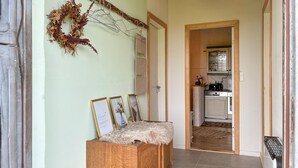 Un couloir mène à une cuisine où l’on trouve un banc en bois rustique, des tableaux encadrés et une guirlande décorative.