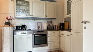 Une cuisine avec des meubles blancs, une cuisinière Bosch, un four Siemens et divers ustensiles de cuisine disposés sur le plan de travail.