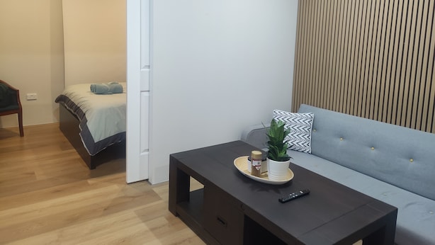 Une chambre moderne avec un lit, un canapé, une petite table agrémentée d’une plante et d’un plateau, et un plancher en bois.