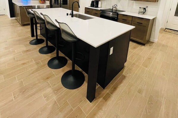 A modern kitchen with a white countertop, black bar stools, and a stainless steel sink.