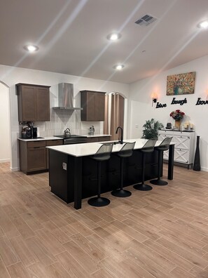 A modern kitchen with a central island, bar stools, and a coffee machine.