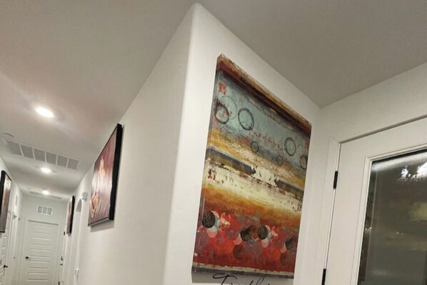 A hallway with a painting on the wall, a door, and a light fixture on the ceiling.