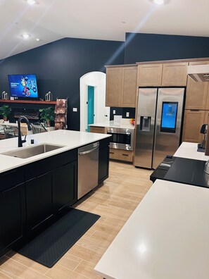 A modern kitchen with a central island, stainless steel appliances, and a flat-screen TV on the wall.