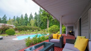 Un patio extérieur couvert avec une piscine, des meubles en osier et une table en verre.