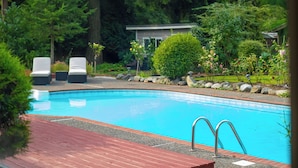 Une piscine dotée d’une terrasse en bois, entourée d’une végétation luxuriante et d’arbres.