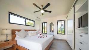 Une chambre à coucher comprenant un lit, une table de chevet, un ventilateur de plafond, de grandes fenêtres et un téléviseur intégré.
