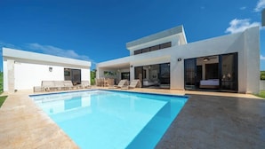 Une maison moderne dotée d’une piscine, d’un espace salon extérieur et d’un patio couvert.