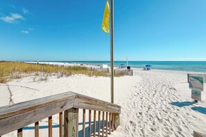 Ein sandiger Strand mit einer Holzpromenade, einer Flagge und einem Schild.