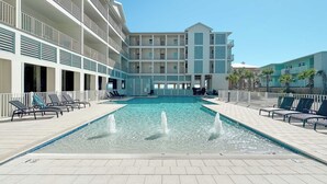 Et poolområde med en rektangulær pool, liggestole og en bygning med flere etager og balkoner.