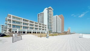 Et hotel ved stranden med flere etager, en sandstrand foran og en klar blå himmel.
