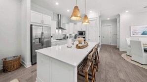 A modern kitchen with white cabinetry, stainless steel appliances, and a central island with bar stools.