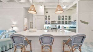 A kitchen with white cabinets, a central island with bar stools, and hanging wicker pendant lights. - Salt & Sunset by Stay on 30a (Watercolor)