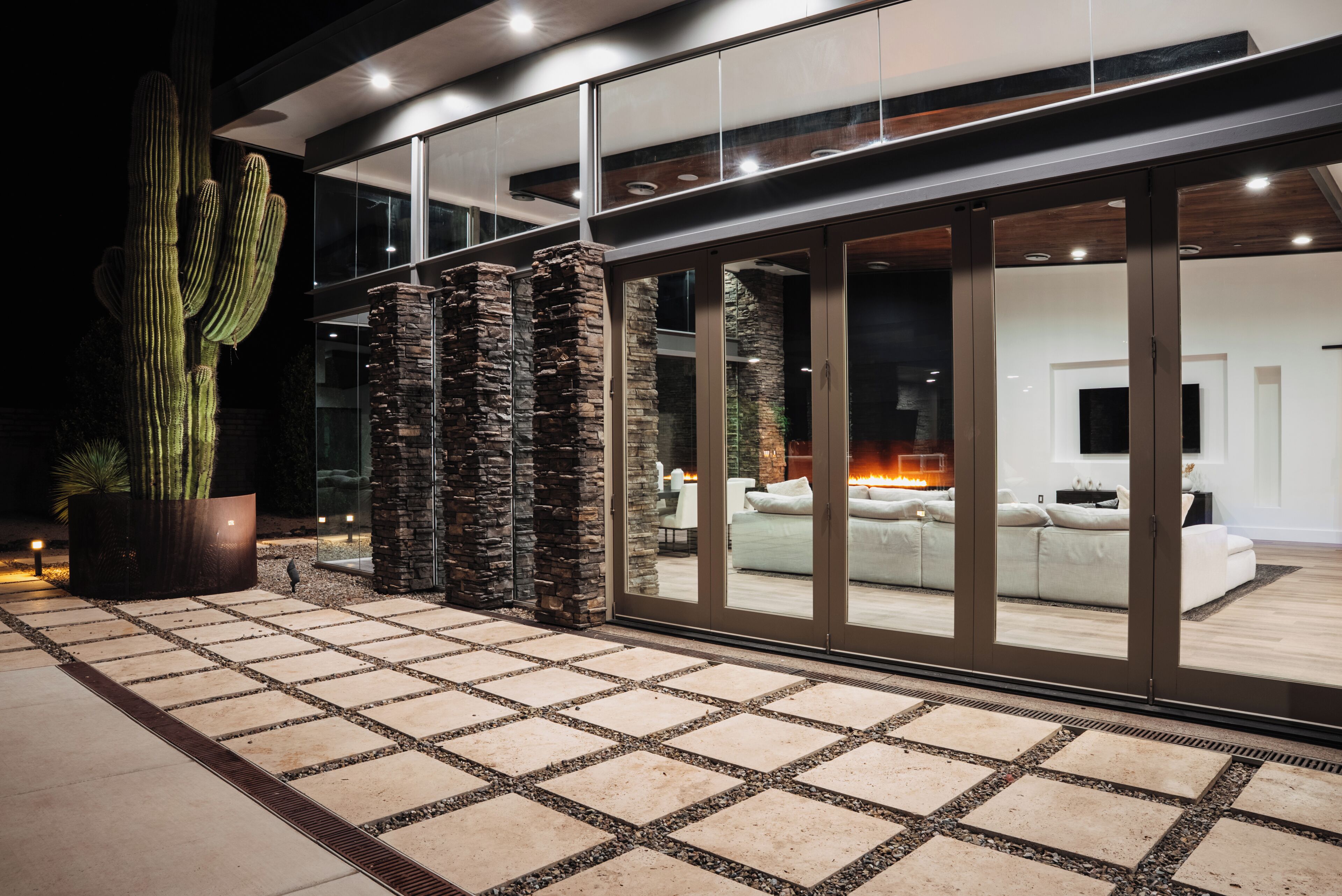 A modern house with a large glass door leading to a living area with a fireplace.