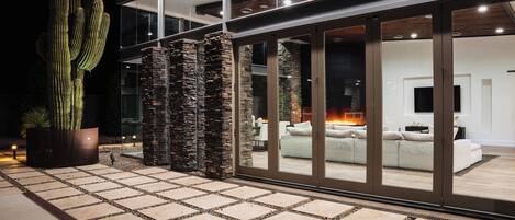 A modern house with a large glass door leading to a living area with a fireplace.