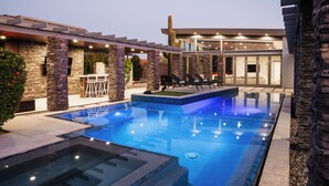 Ein moderner Poolbereich im Freien mit Steinpfeilern, Liegestühlen und einer gut beleuchteten Terrasse.