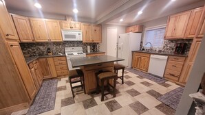 Eine moderne Küche mit Holzschränken, einer zentralen Kochinsel mit Hockern, einer Mikrowelle, einem Herd, einem Kühlschrank und einem Geschirrspüler.