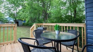 A covered outdoor patio with a round table and four chairs, surrounded by a wooden deck and a railing. - Division Ave East Lake Update (Birmingham)