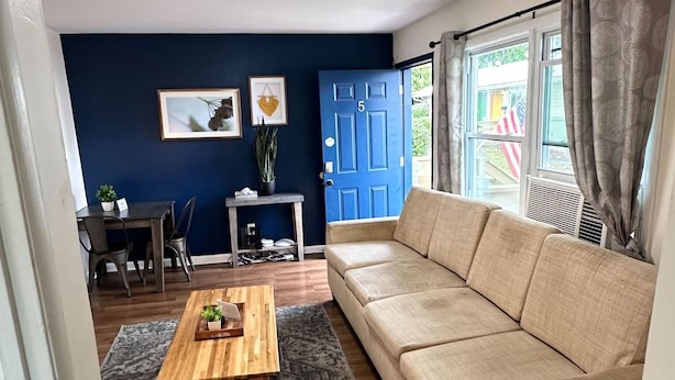 A living room with a beige sofa, a wooden coffee table, and a blue door. - 12th Ave The Bricks - Unit 5 (Birmingham)