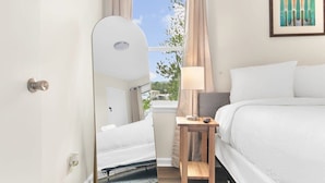 A hotel room with a bed, a bedside table with a lamp, a large mirror, and a window with curtains. - 12th Ave The Bricks - Unit 5 (Birmingham)
