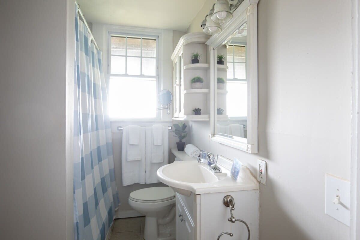 A small, white bathroom with a toilet, sink, and shelves above the mirror.