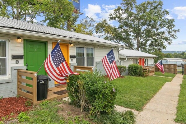 A small, single-story building with a green door and windows. There are two American flags displayed outside. - 12th Ave The Bricks - Unit 3 (Birmingham)