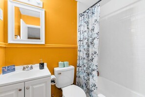 A bathroom with a white sink, a toilet, a shower curtain with a floral pattern, and a mirror above the sink. - 12th Ave The Bricks - Unit 3 (Birmingham)