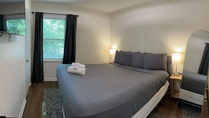 Ein Schlafzimmer mit einem Bett, Nachttischlampen, einem Fenster mit Vorhängen, einem Spiegel und einem kleinen Tisch.