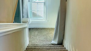 Un escalier recouvert de moquette, avec un mur blanc et une fenêtre en haut.