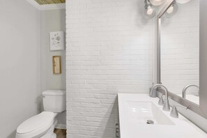 A modern bathroom with a white brick wall, a white toilet, and a white sink with a mirror above it. - 86th Cozy Coop (Birmingham)