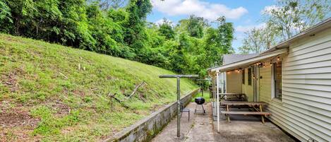 A covered outdoor area with picnic tables and a barbecue grill, adjacent to a building with a porch.