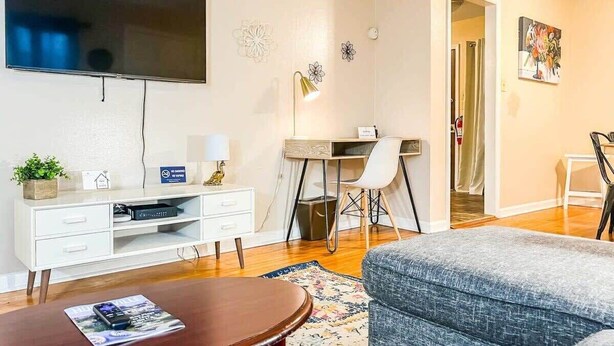 A living room with a flat-screen TV, a desk with a chair, a sofa, and a dining table with chairs.