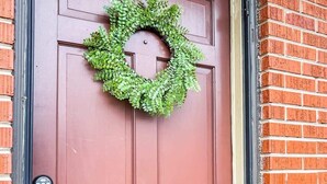A red door with a green wreath, a keypad lock, and a yellow security device.