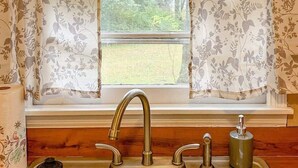 A kitchen with a double stainless steel sink, wooden countertop, and a window with floral curtains.