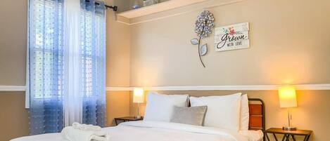 A neatly made bed with white linens, a decorative wall piece, and a bedside lamp.