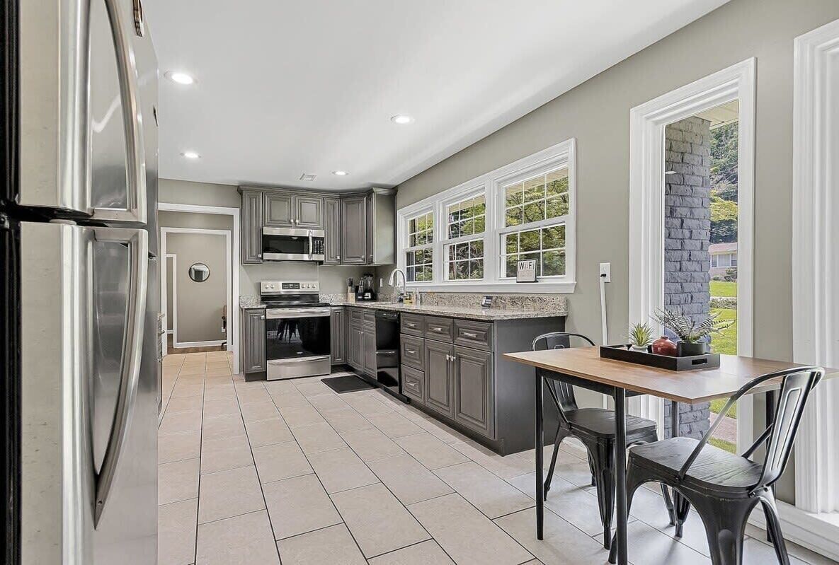 A modern kitchen with grey cabinets, stainless steel appliances, and a dining area with a wooden table and chairs.