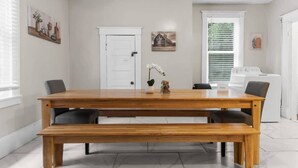 A dining area with a wooden table and benches, a white door, and a window with blinds. - 29th Street Ensley Heights Hideaway 1 (Birmingham)