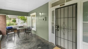 A covered patio area with a table and chairs, a grill, and a door with a decorative metal gate. - 29th Street Ensley Heights Hideaway 1 (Birmingham)
