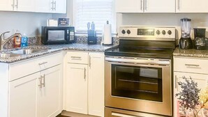 A kitchen with white cabinets, a stainless steel oven, a microwave, and a blender.
