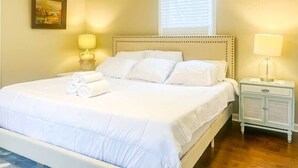 A neatly made bed with white linens and rolled towels, a bedside lamp, and a nightstand with a lamp.
