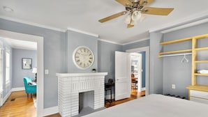 A bedroom with a white bed, a white fireplace, a clock on the wall, and a ceiling fan. - 49th Terrace Haven (Birmingham)