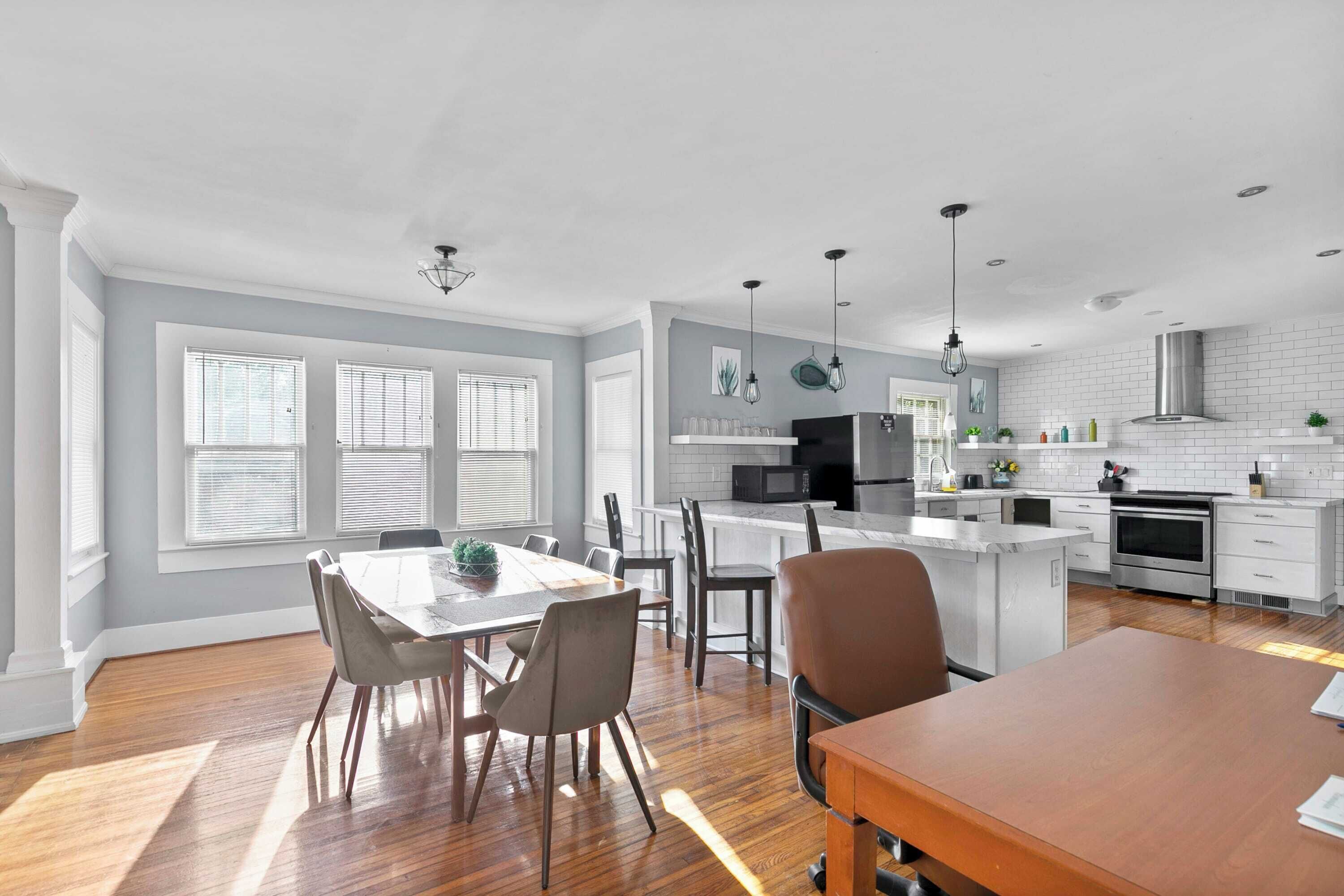 A modern kitchen with white cabinetry, a central island, and a dining area with a wooden table and chairs.