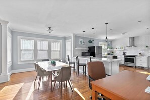 A modern kitchen with white cabinetry, a central island, and a dining area with a wooden table and chairs.