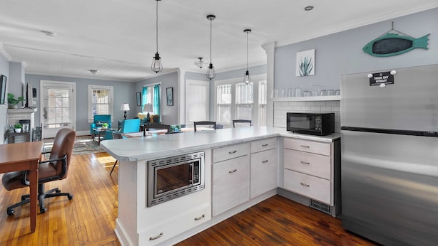 A modern kitchen with white cabinetry, a stainless steel refrigerator, and a built-in microwave. There is a dining area with a wooden table and chairs. - 49th Terrace Haven (Birmingham)