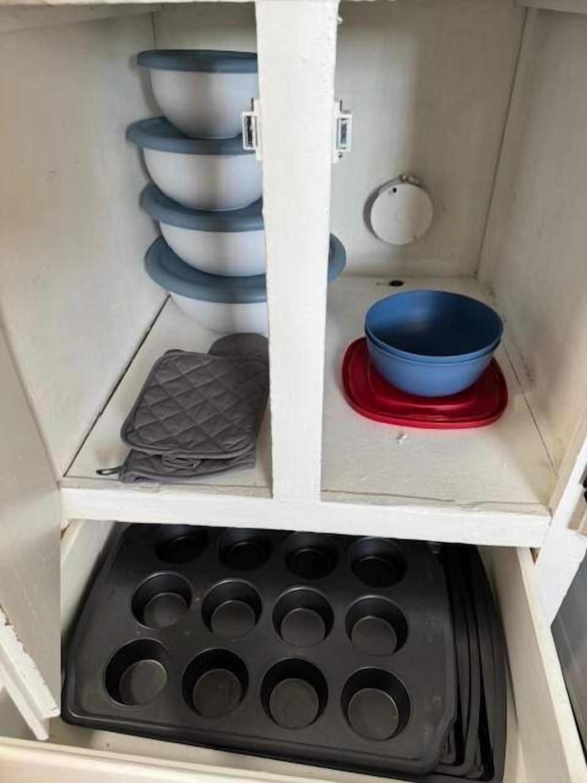 Una cocina con un armario blanco, un tazón azul sobre una bandeja roja, un molde para muffins negro y tazones apilados.