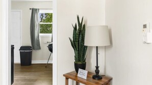 Um corredor com uma planta em vaso, uma luminária e uma placa sobre uma mesa de madeira.