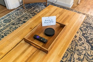 A wooden coffee table with a tray containing a remote control and a speaker, and a sign thanking guests for staying.