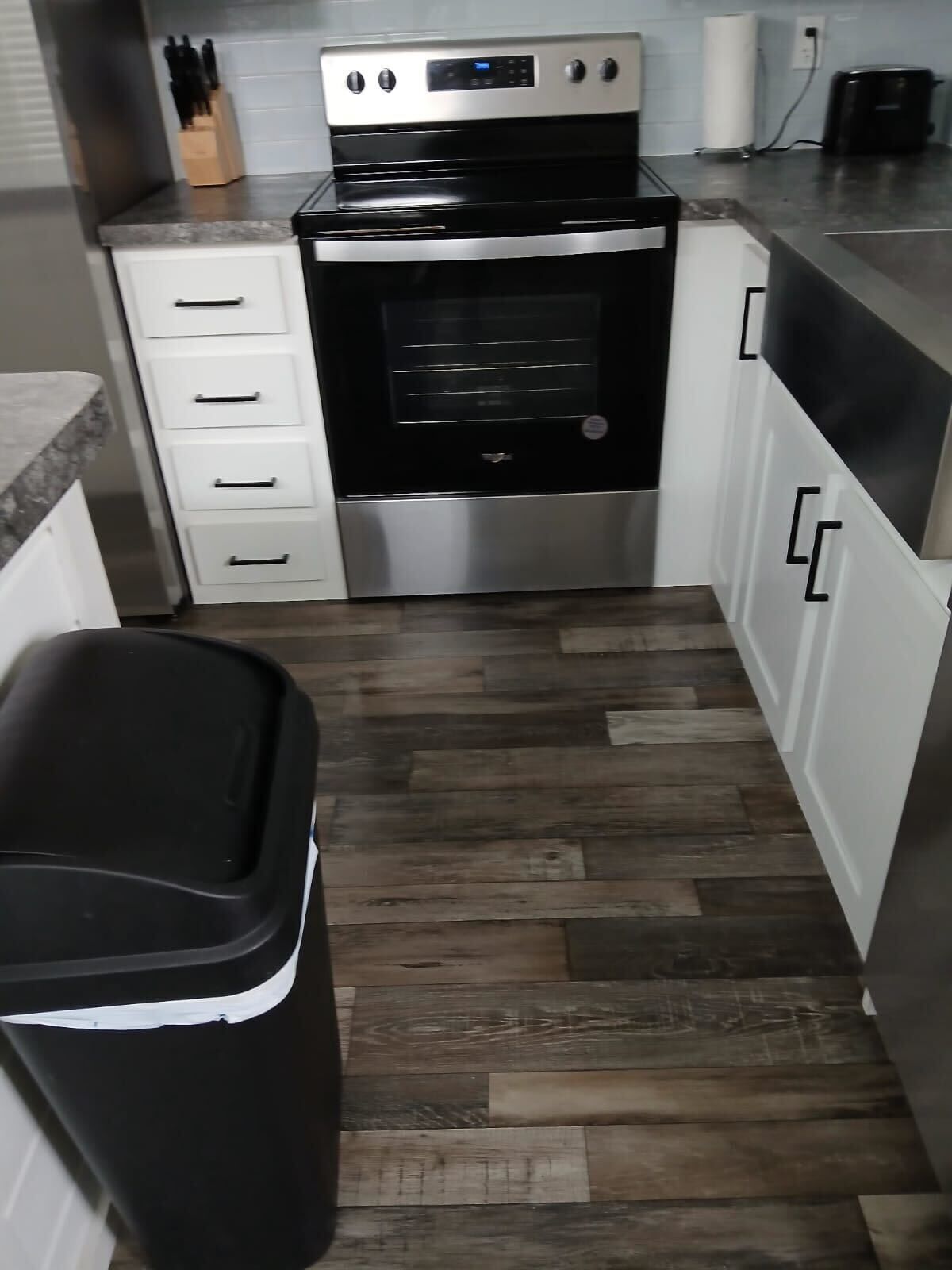 A kitchen with a stainless steel oven, white cabinets, and a wooden floor.