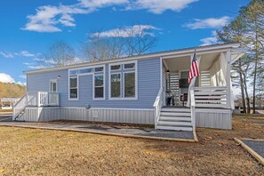 A single-story, light blue building with a covered porch and a small staircase leading to a deck.