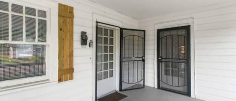 Fachada blanca con dos puertas negras, una puerta de madera y un ventanal con contraventanas.
